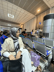 a woman in a hijab sits in a waiting area at an airport with a sign that says ' a ' on it