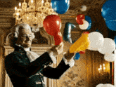 a man in a wig is blowing up balloons in a room with a chandelier