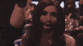 a man with a beard is surrounded by people applauding and laughing
