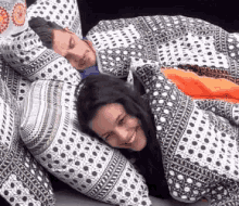 a man and a woman are laying under a blanket and smiling .