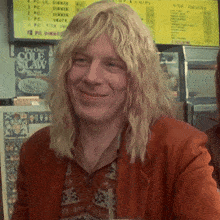 a man with blonde hair is smiling in front of a sign that says try our code slaw