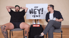two men are sitting in front of a sign that says hey ( ew )