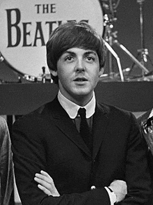 a man in a suit and tie is standing with his arms crossed in front of a drum .