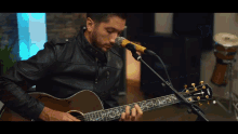 a man in a denim shirt is playing an acoustic guitar in front of a microphone