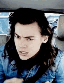 a man with long hair is wearing a blue shirt and a seat belt