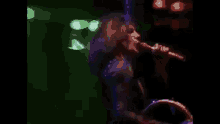 a woman is singing into a microphone on a stage in front of a green light .