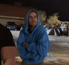 a man in a blue hoodie is standing in a parking lot .