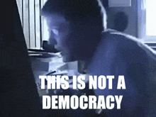 a man looking at a computer screen with the words " this is not a democracy " on the bottom