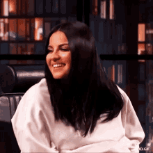 a woman is smiling while sitting in a chair in front of a bookshelf .