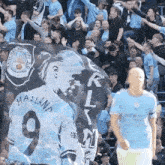 a man wearing a number 9 jersey stands in front of a manchester city fc banner
