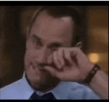 a man in a blue shirt and tie wipes his eyes with his hand