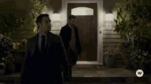 two men are standing in front of a house with the letter w on the bottom