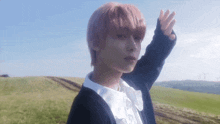 a young man with pink hair is standing in a field with his hand outstretched .