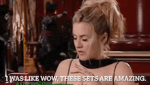 a woman is sitting at a table with her hands on her chest and says `` i was like wow , these sets are amazing ''