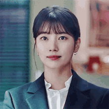 a close up of a woman wearing a suit and earrings looking at the camera .