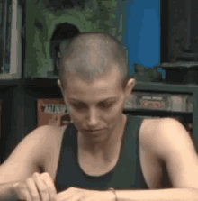a woman with a shaved head is sitting at a table with her hands on her wrist .
