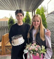 a boy and a girl are holding a cake and flowers .