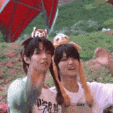 two young men wearing stuffed animals on their heads are standing next to each other in a park .
