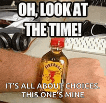 a bottle of fireball sits on someone 's wrist in front of a keyboard