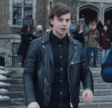 a young man in a black leather jacket stands in front of a crowd