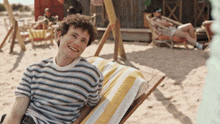 a man in a striped shirt is sitting in a chair on the beach