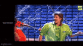a man in a green shirt is standing next to a woman in a red dress in front of a blue wall .