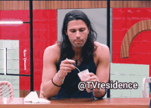 a man with long hair is sitting at a table with a spoon in his hand and the words @tvresidence above him