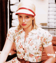 a woman wearing a straw hat and a floral shirt is sitting on a bed with a global hd logo in the corner