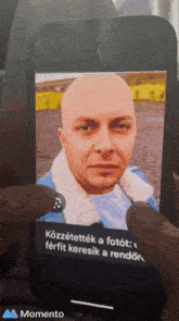 a person is holding a cell phone with a picture of a bald man on the screen
