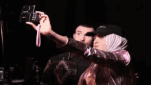 a man and a woman are taking a selfie with a camera . the woman is wearing a hijab .