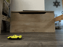 a yellow toy car is sitting on the floor next to a wooden box