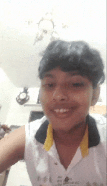 a young boy wearing a white shirt with a yellow collar is smiling .