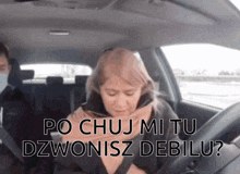 a woman is sitting in a car with the words po chuj mi tu dzwonisz debilu