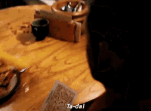a person is sitting at a table holding a card that says ta-dal