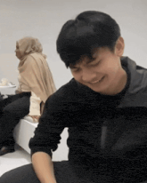 a man in a black jacket is smiling while a woman sits behind him