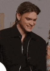 a man in a black jacket is smiling and holding a pair of sunglasses .