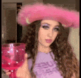 a woman wearing a pink cowboy hat is holding a pink glass .