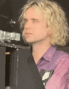 a man with blonde curly hair is wearing a purple striped shirt