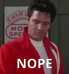 a man in a red jacket is standing in front of a sign that says ' nope ' on it .