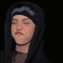 a woman wearing a black hoodie and a black hat is making a funny face .