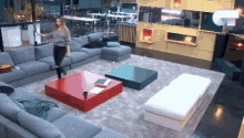 a woman stands on a red coffee table in a living room filled with furniture