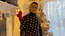 a man wearing a santa hat stands in front of a christmas tree and a sign that says merry christmas
