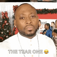 a man with a beard and a necklace is standing in front of a christmas tree and making a funny face .