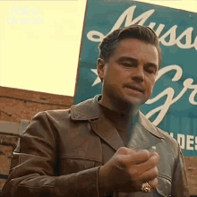 a man in a leather jacket is standing in front of a blue sign .