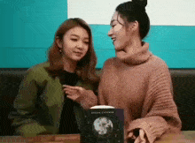 two women are sitting at a table talking to each other and holding hands .