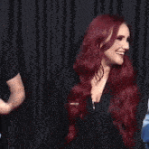 a woman with long red hair is laughing and covering her mouth with her hand .