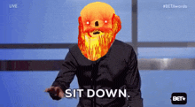 a man with a flaming beard says sit down in front of a microphone
