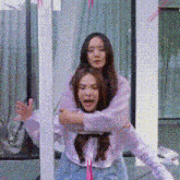 two women are standing next to each other and one of them is holding the other on her back .
