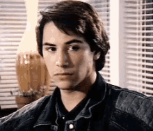 a young man wearing a denim jacket is sitting in front of a window .