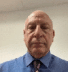 a bald man in a blue shirt and tie is taking a selfie .